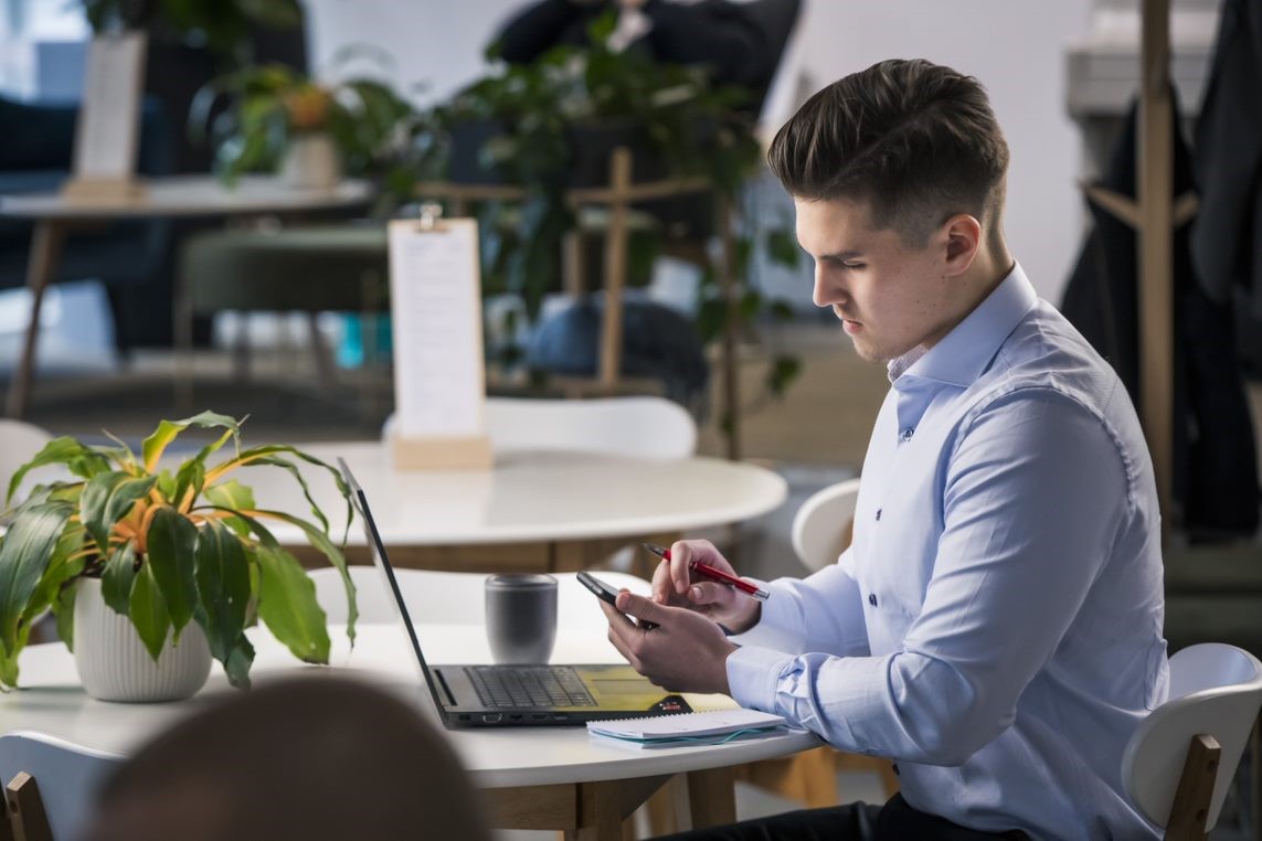 Nuori mies selaa puhelinta työpöydän ääressä